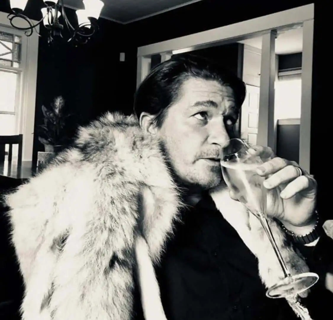 A person wearing a fur coat drinks from a cocktail glass.