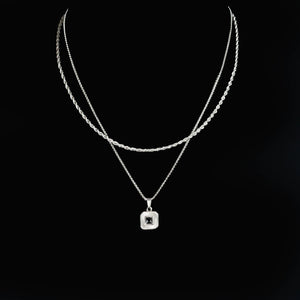 Layered silver necklace with a square pendant featuring a central gemstone.