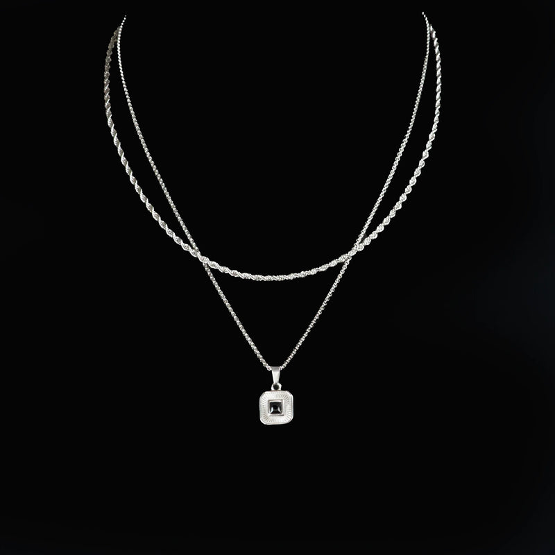 Layered silver necklace with a square pendant featuring a central gemstone.