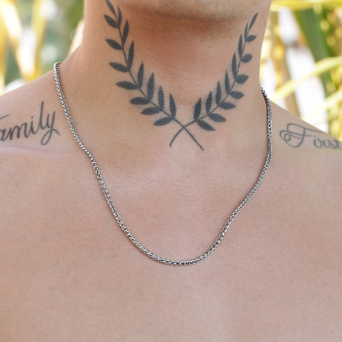 Silver chain necklace worn with a laurel wreath neck tattoo visible beneath it.