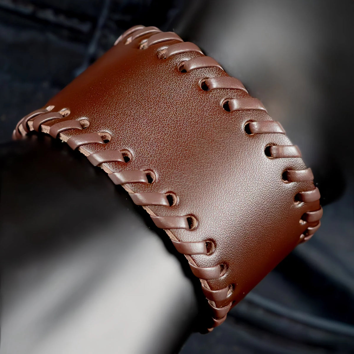 Brown leather cuff bracelet with decorative lacing along the edges.