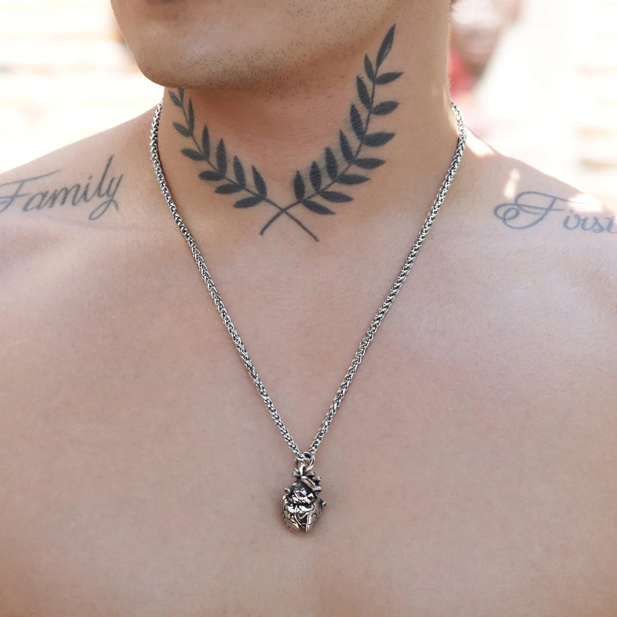 Necklace with a pendant worn over a tattoo of laurel branches on the neck.