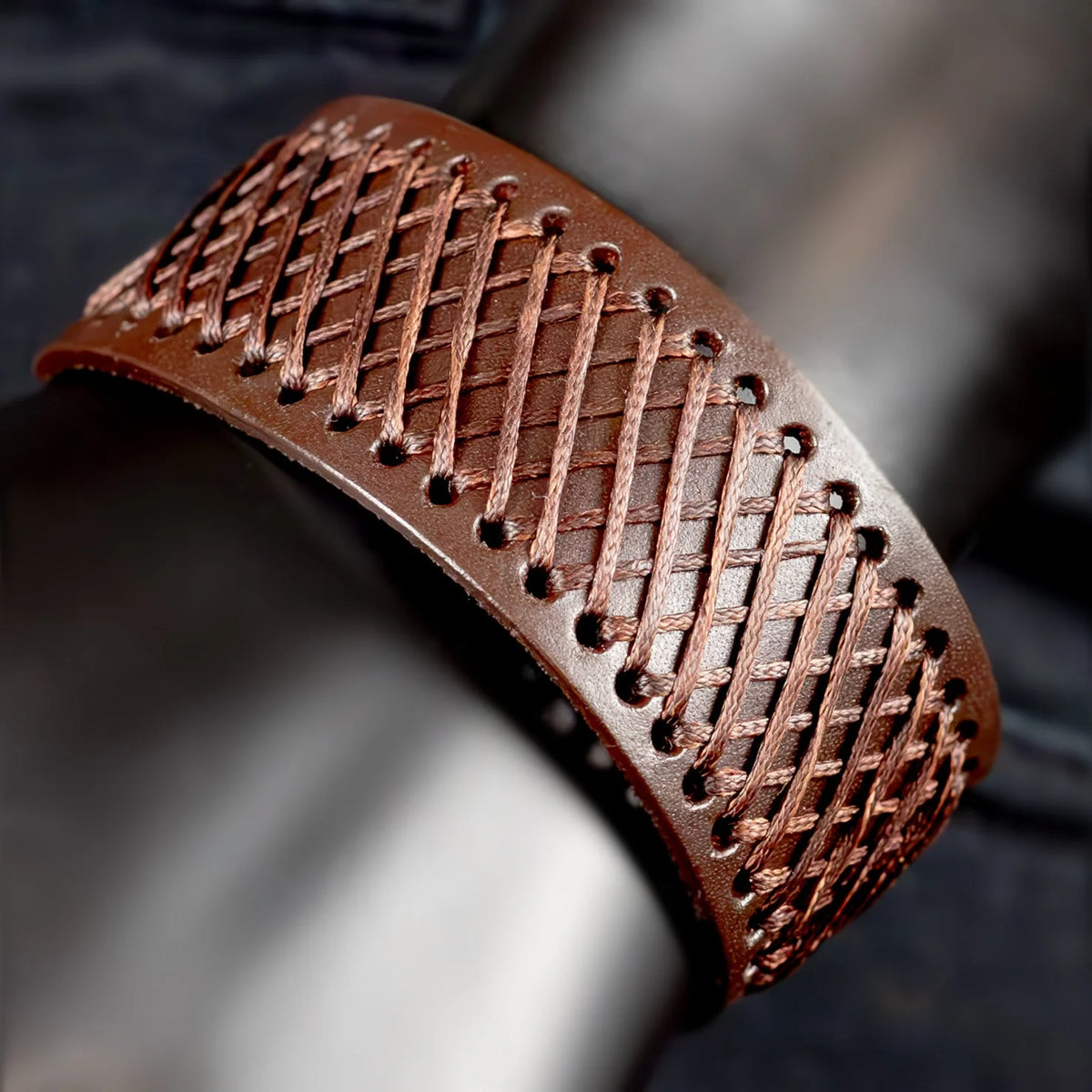 Brown leather bracelet with intricate cross-stitched pattern.