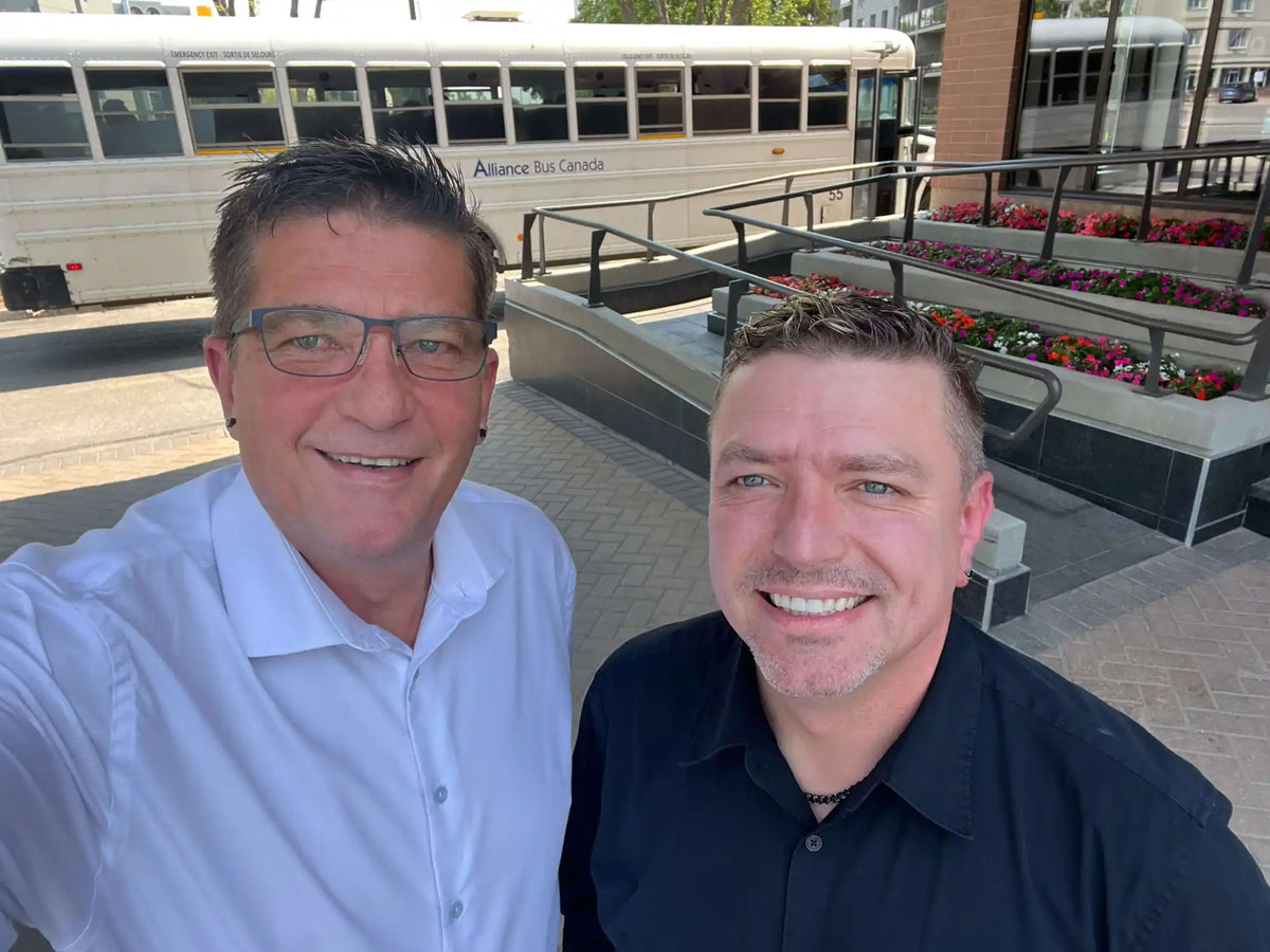 A selfie of two smiling men wearing glasses and collared shirts.