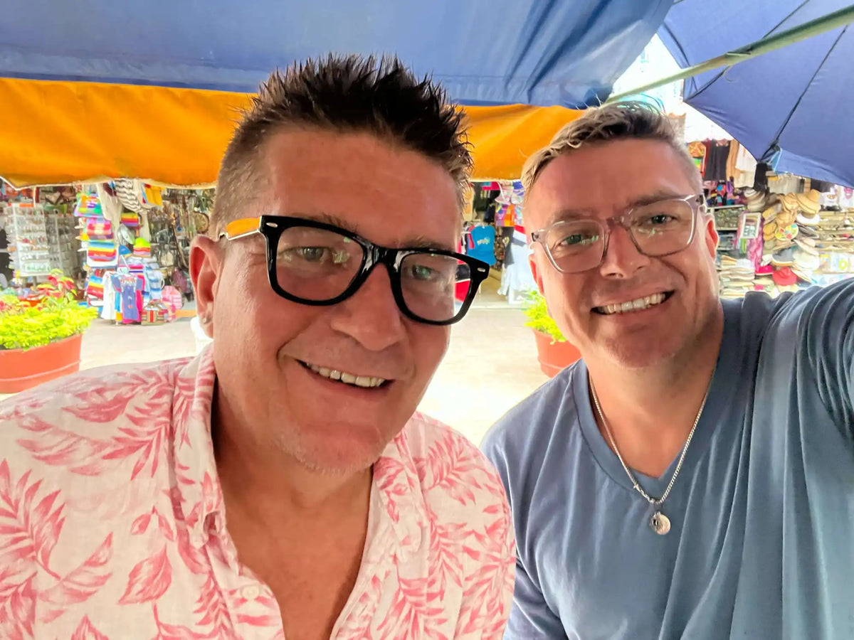 A selfie of two smiling people wearing glasses at what appears to be an outdoor market.