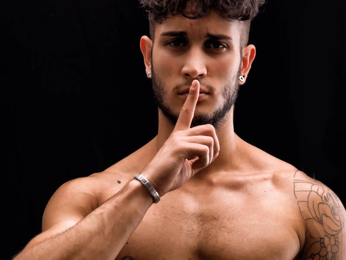 A shirtless person making a ’quiet’ gesture with their finger pressed to their lips.