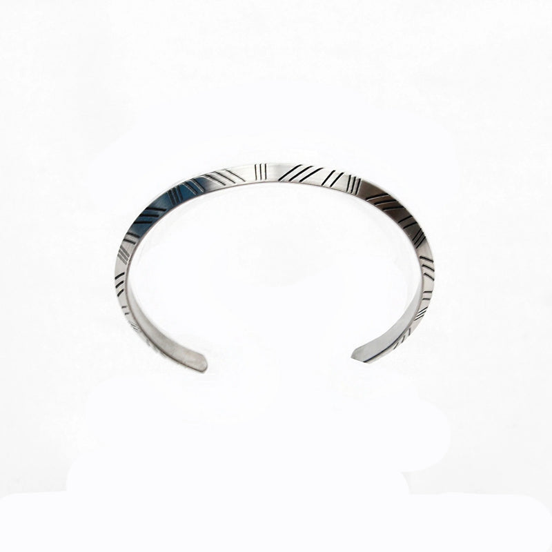 Silver cuff bracelet with engraved linear patterns.