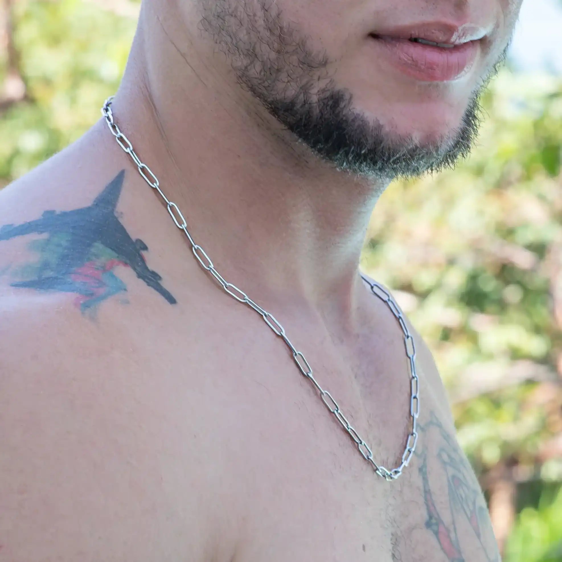 Silver chain necklace worn by a person with visible tattoos and facial hair.