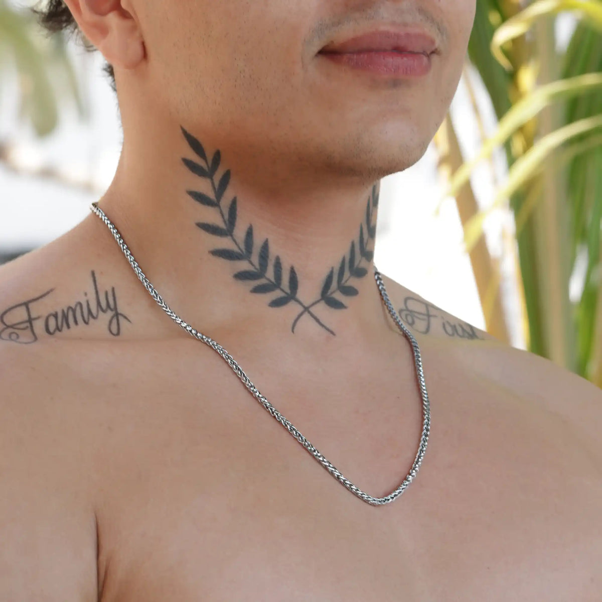 Neck tattoo of crossed laurel branches above a silver chain necklace.