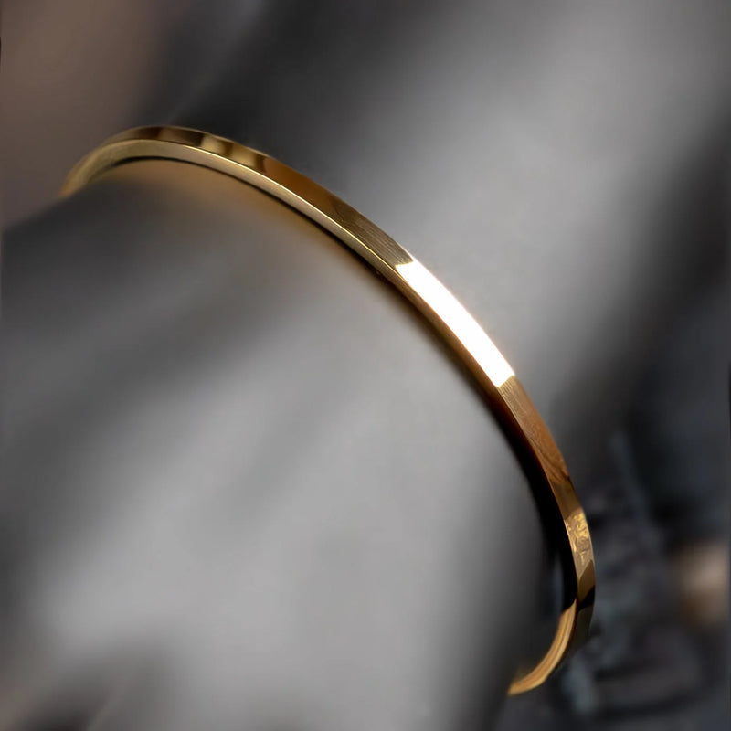 Thin, curved gold bracelet or bangle with a polished surface.