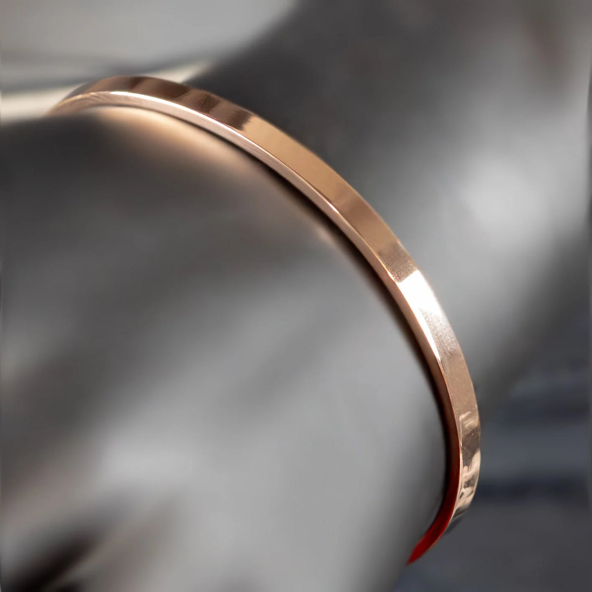 Rose gold metal bracelet or bangle with a sleek, curved design.