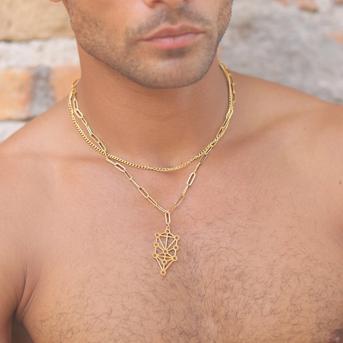 Gold necklace with a geometric pendant worn around a person’s neck.