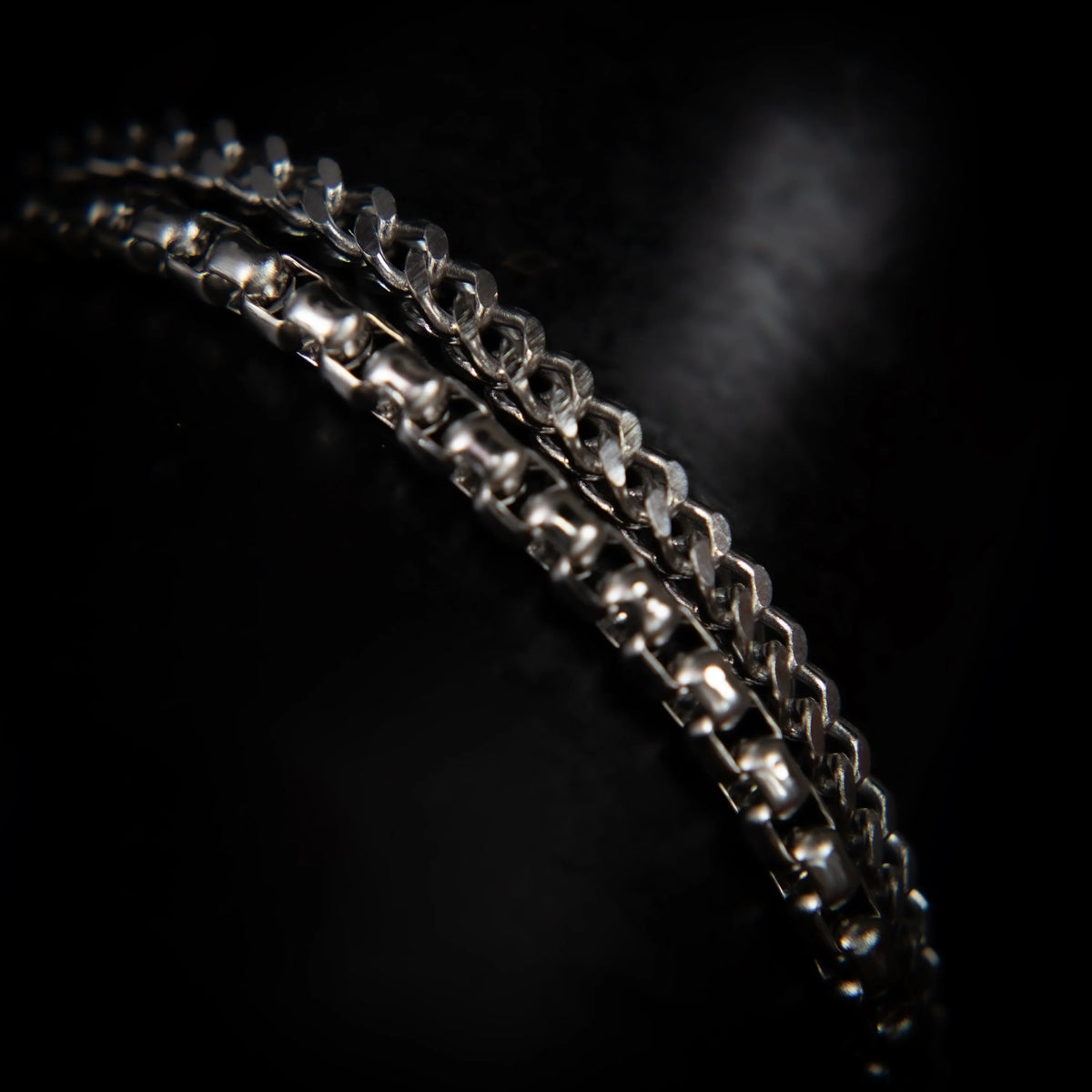 Curved silver chain or bracelet with intricate links and reflective surfaces.