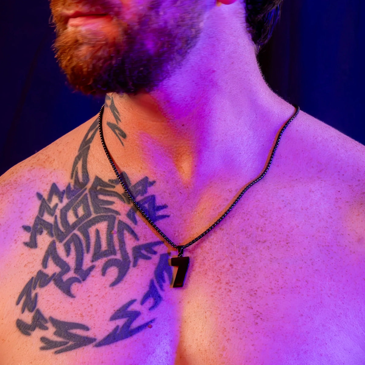 Tribal-style black tattoo on a shoulder illuminated by purple lighting.